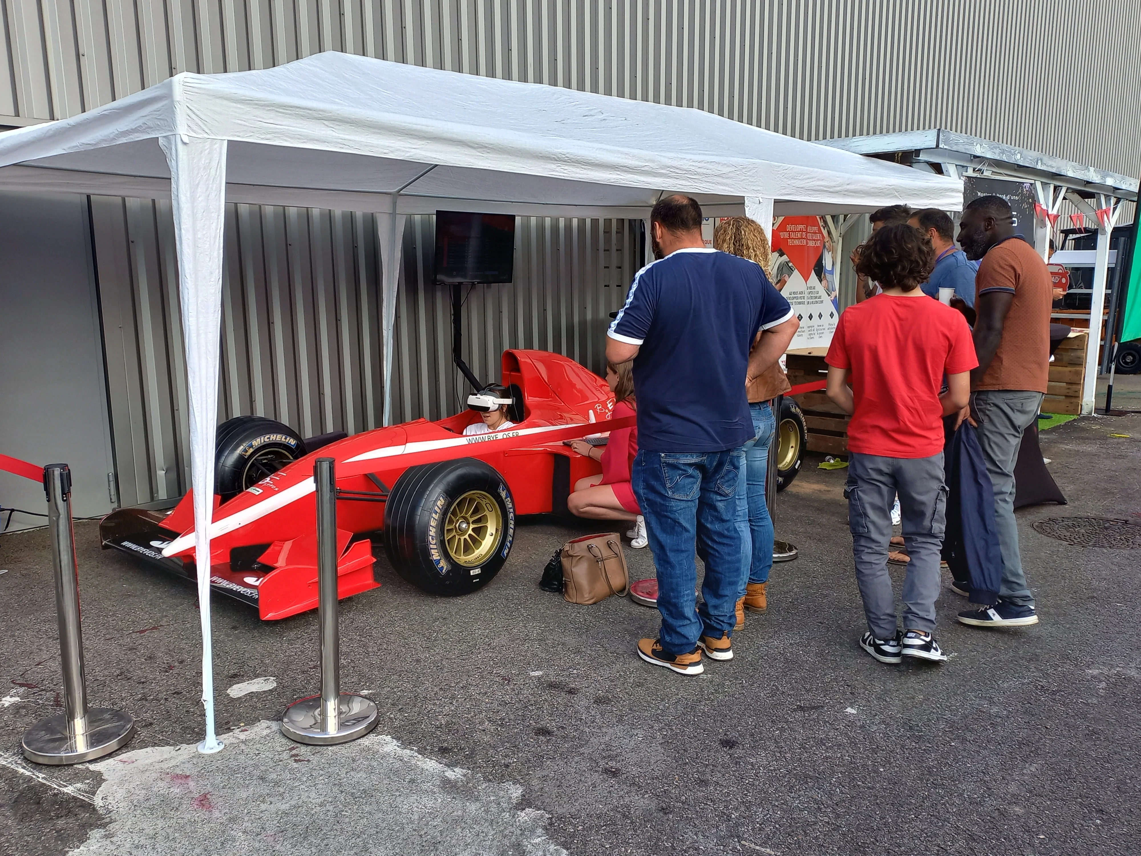 Monoplace rouge sous une tente, personne en casque VR, spectateurs autour